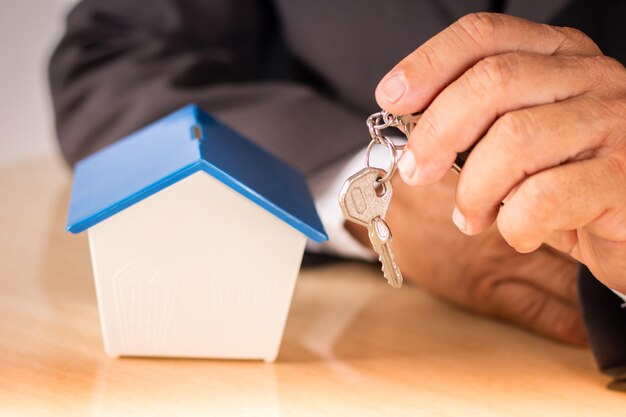 Business man holding key with small house on table. housing concept.