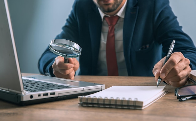 Business man holding magnifier with laptop