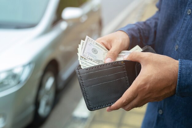 L'uomo di affari che tiene i soldi in mano sta davanti all'automobile prepara la paga a rate