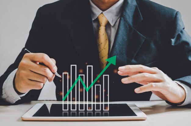 Photo business man holding pen bar graph and green arrow on tablet at desk.