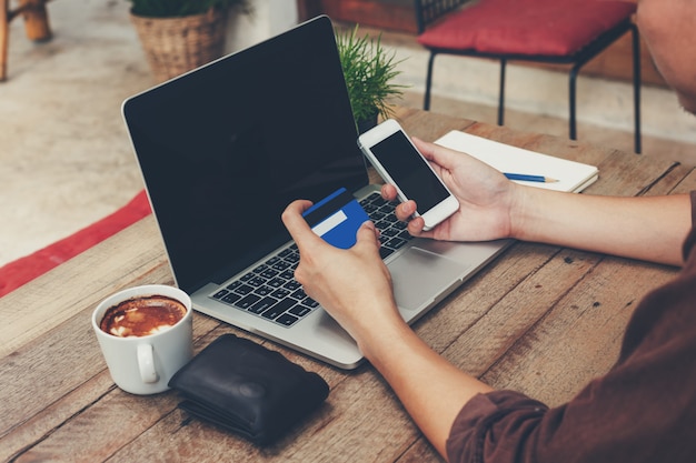 Photo business man holding phone and payment credit card with laptop on wooden table.