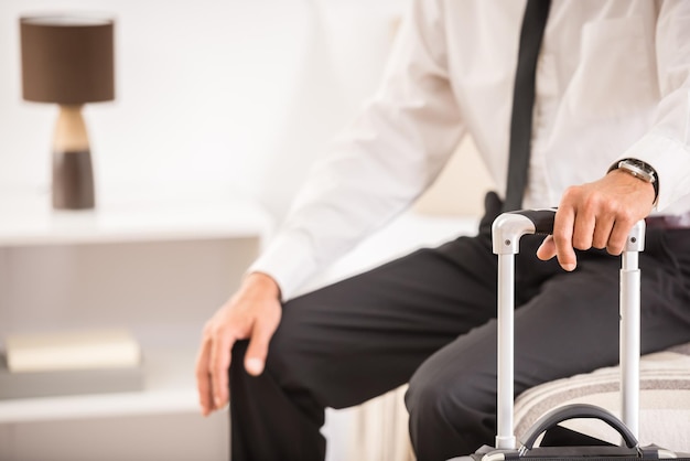 Business man holding suitcase while sitting on bed at the hotel room Closeup