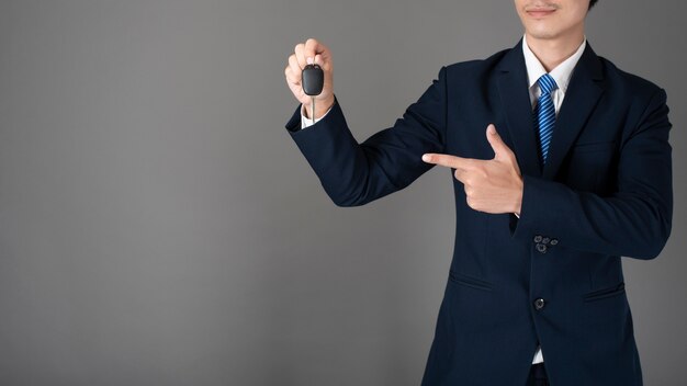 Business man is holding car key, grey background in studio