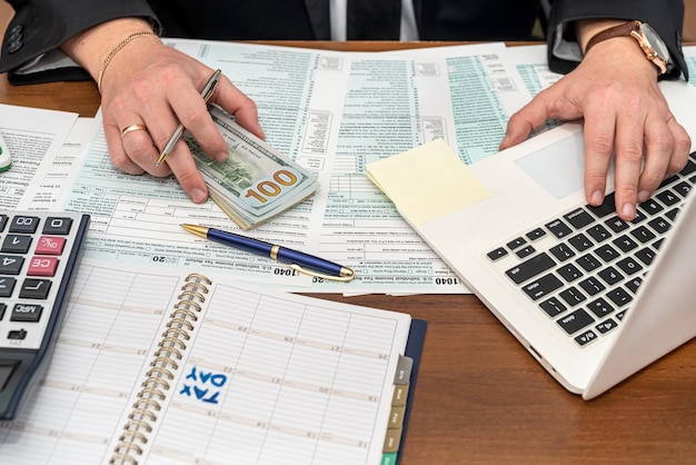 a business man in a jacket fills out tax forms and makes calculations at the table. Business and tax forms concept