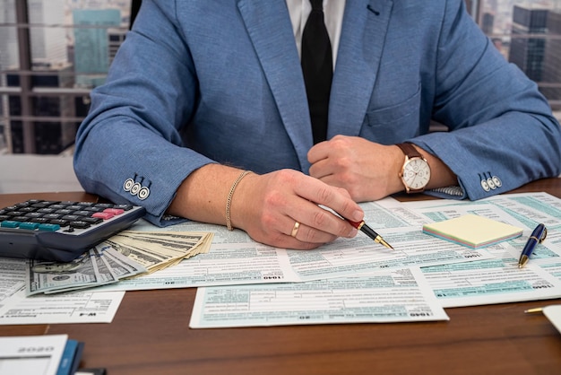 A business man in a jacket fills out tax forms and makes calculations at the table Business and tax forms concept