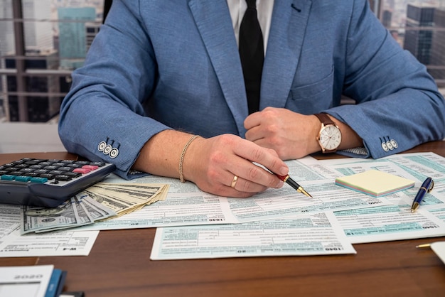 A business man in a jacket fills out tax forms and makes
calculations at the table business and tax forms concept