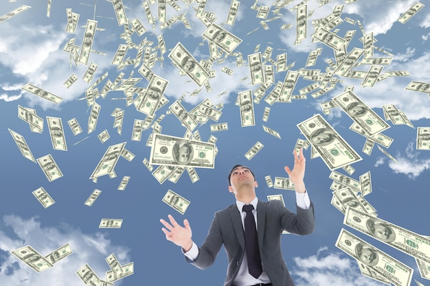 Business man looking at money rain against sky with clouds