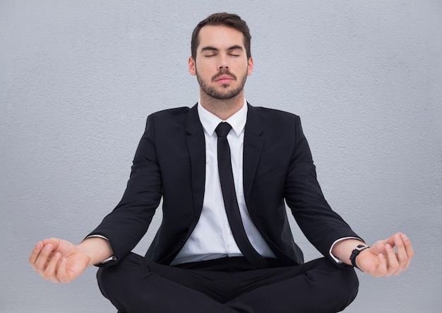 Business man meditating against grey wall