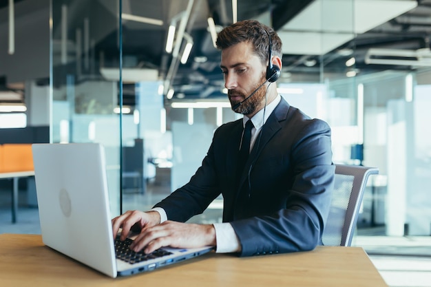 Business man in a modern office works at a computer uses a headset for video calling technical support