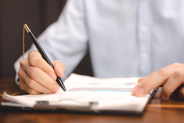 Business man person using a pen to sign a agreement document
paper to approve by signature hand of businessman working on
finance lawyer contract paperwork in office concept of deal on
business desk