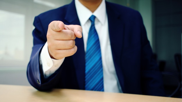 Business man pointing finger at you at desk