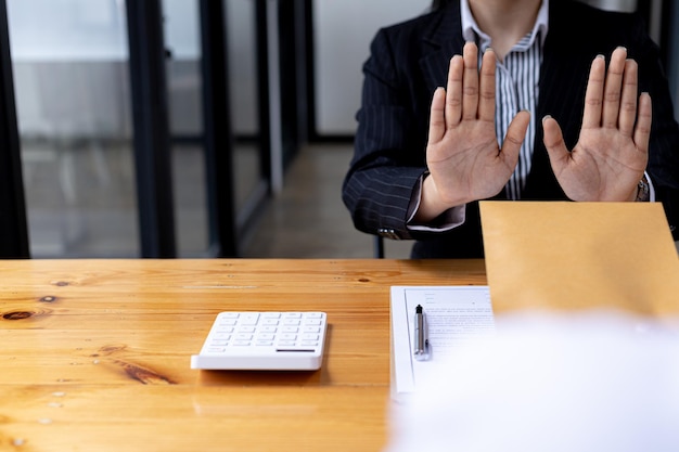 Business man raised her hand to deny accepting a bribe from a business partner, a brown envelope containing a large number of dollar bills as money for bribery, a corruption concept.