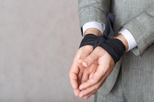 Business man's hands tied with black fabric. Closeup