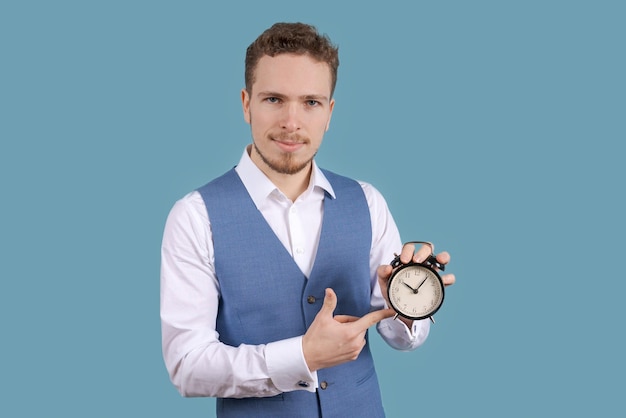 Business man in shirt and blue vest holding an alarm clock on blue background