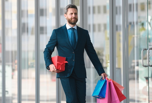 Foto uomo d'affari shopping in un centro commerciale uomo d'affari felice in tuta tenendo sacchetti di carta shopping