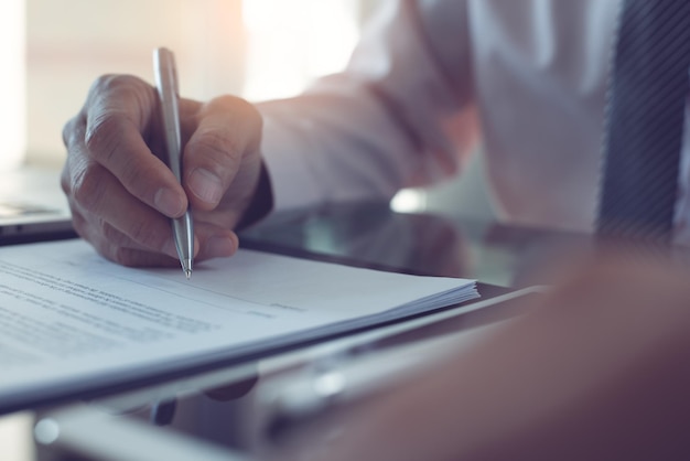 Business man signing official contract with a pen on desk in modern office close up