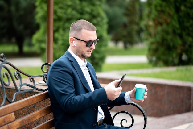 A business man sits on a bench drinks coffee and talks on the phone Break Lunch