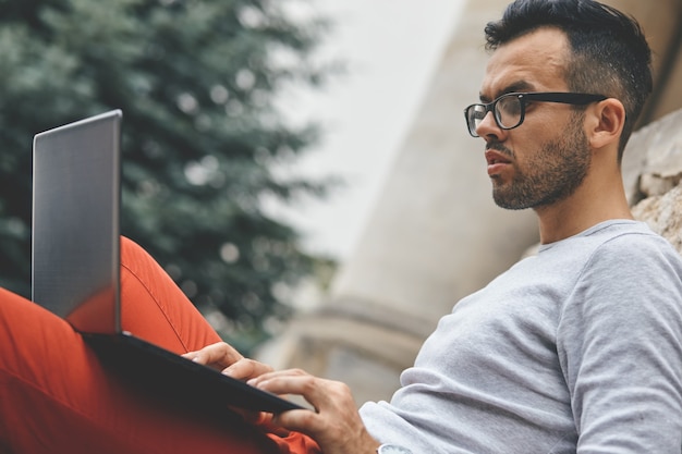 Business man sitting on the bench and watching on the laptop in city park outdoors