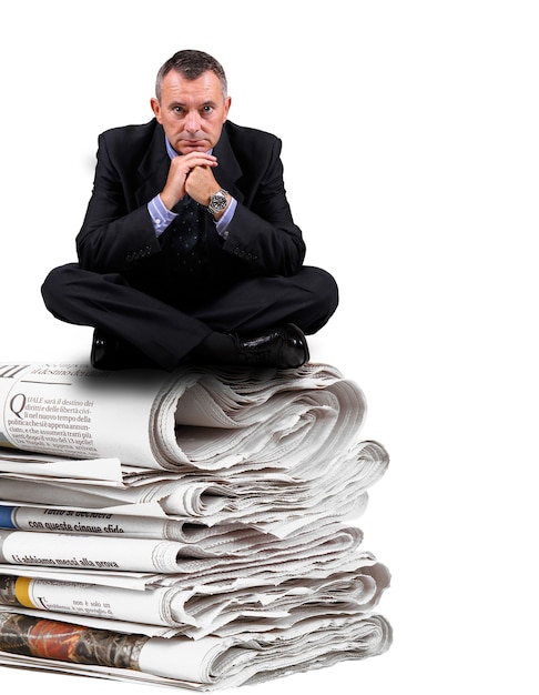 Business man sitting on newspaper stack isolated on white background