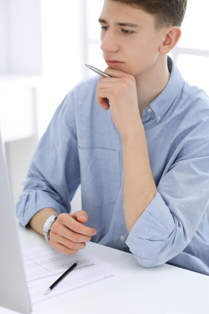 Business man sitting and working with computer and calculator\
in white office student guy studying at home or young accountant\
checking balance tax audit and bookkeeping concept