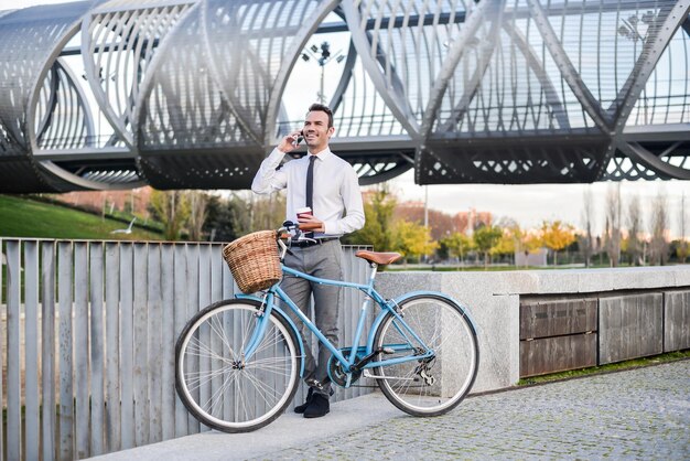 Business man standing by his vintage bicycle speaking on the mobile phone
