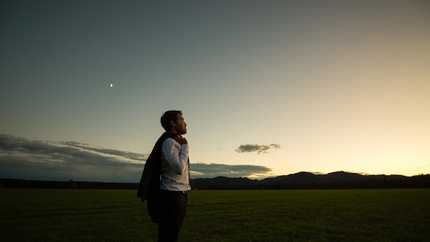 Business man standing outdoors in evening light with his jacket slung over his shoulder