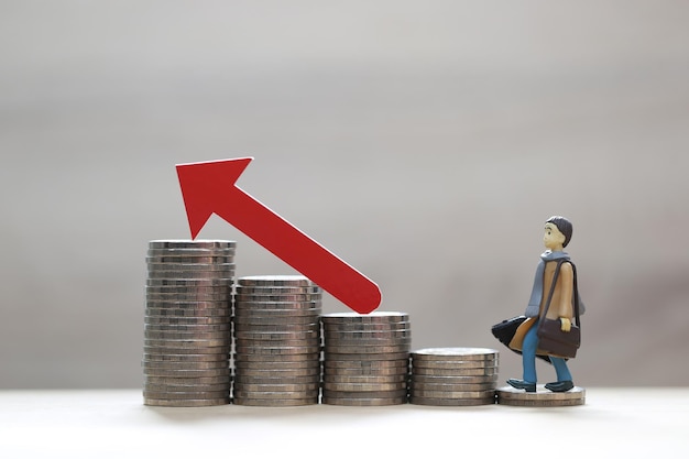 Business man standing on stack of coins money and red arrow graph on natural green background investment and business concept