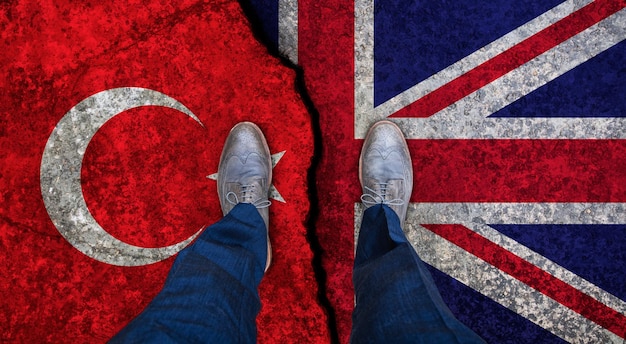 Бизнесмен стоит на треснутом флаге Великобритании и Турции политическая концепция