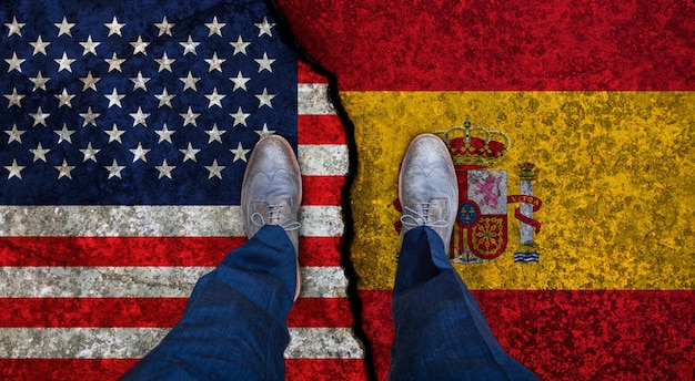 Business man stands on cracked flags of USA and Spain Political concept