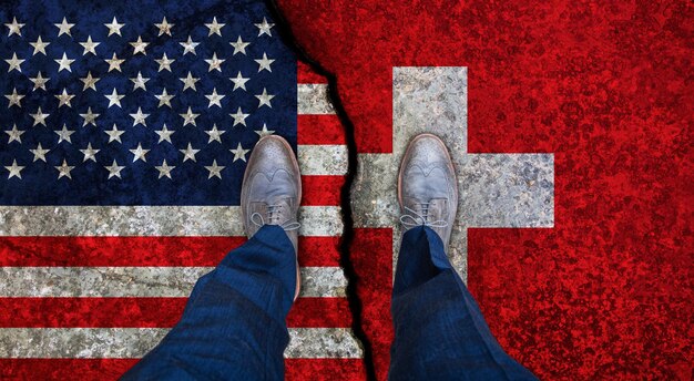 Business man stands on cracked flags of USA and Switzerland Political concept