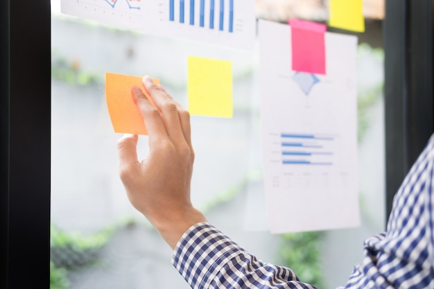 business man sticking adhesive notes on glass wall in office and discussting with team