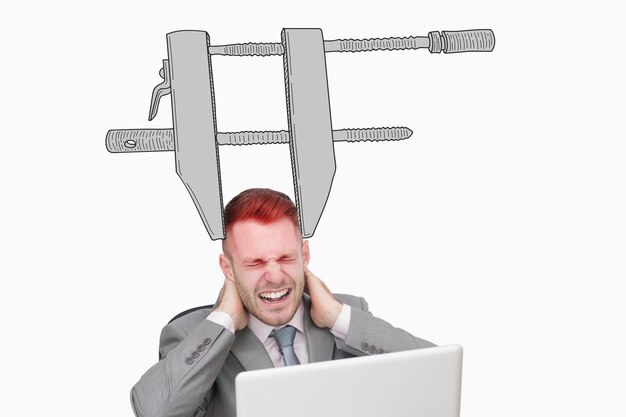 Business man suffering from severe neck pain while using laptop against blue background with vignette