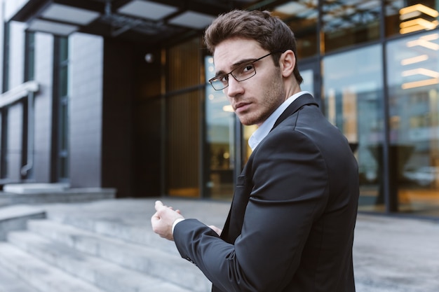 Business man in suit and glasses standing sideways near the office