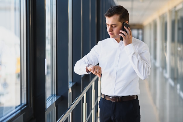 Uomo d'affari in tuta parlando al telefono e guardando lontano vicino alla finestra.