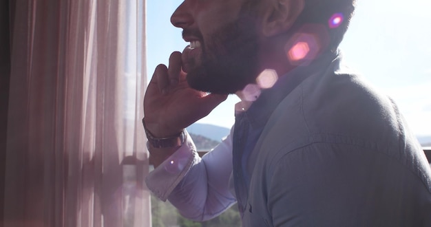 Photo business man talking on cell phone at home with sun flares coming from window