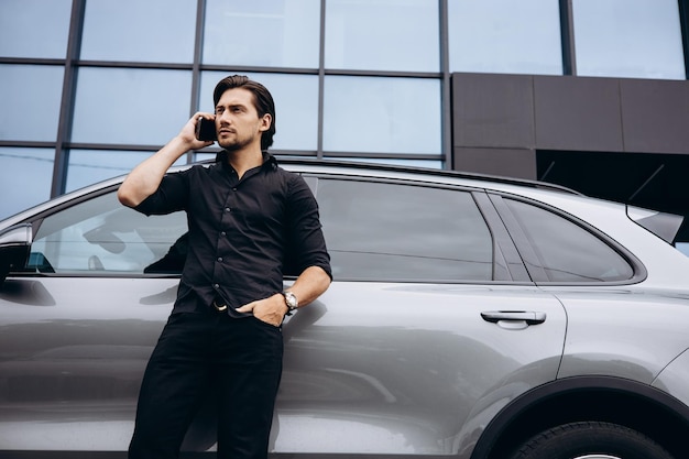 Business man talking on the phone by his car near office building