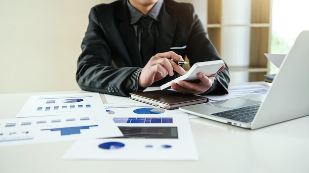 Business man using calculator with computer laptop wearing a black suit politely