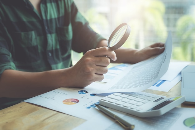 Business man using magnifying to review balance shee