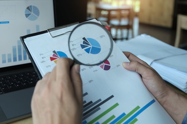 Photo business man using magnifying to review balance sheet annual with using laptop computer