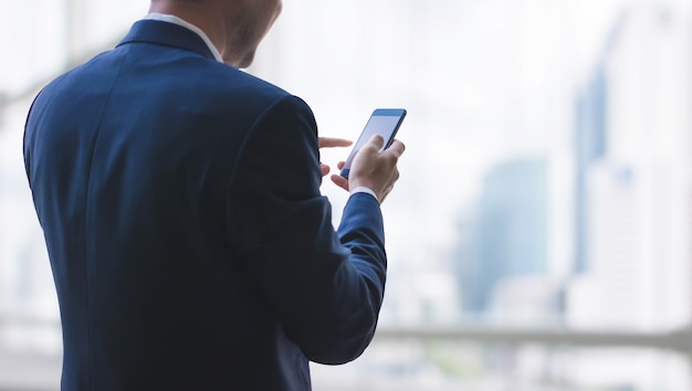 Uomo di affari che per mezzo dello smart phone sulla finestra con il fondo della costruzione della città e lo spazio della copia.