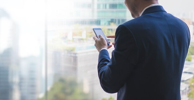 Business man using smart phone on window with city building background and copy space.