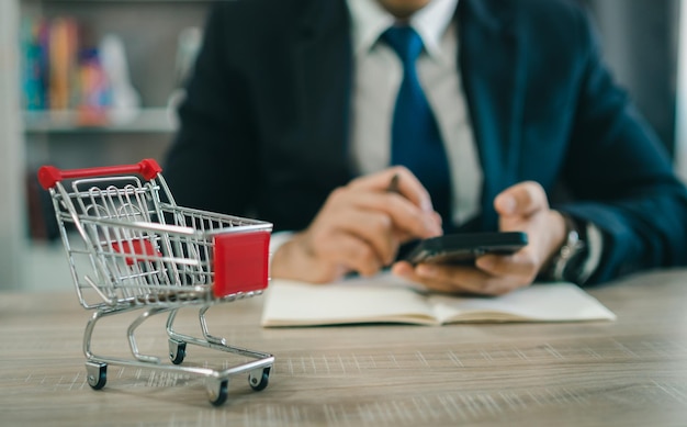 Business man wearing suit and calculates the budget Shopping cart a on table with mobile Budget of poor low income family Rising food and grocery store prices and expensive daily consumer goods