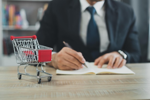 Business man wearing suit and calculates the budget Shopping cart a on table with note book Budget of poor low income family Rising food and grocery store prices and expensive daily consumer goods