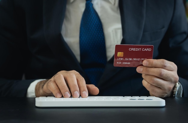 Business man wearing suit and holding credit card and using keyboard computer to shopping online asian man working at home Online shopping ecommerce internet banking spending money