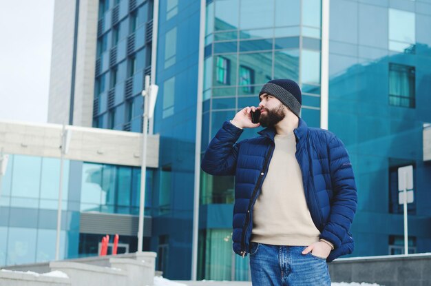 Uomo d'affari in abiti casual invernali, giacca, cappello. camminando per la strada della città, parlando al telefono