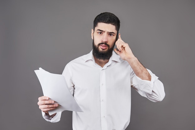 Business man with beard in white shirt holding documents and phone on gray