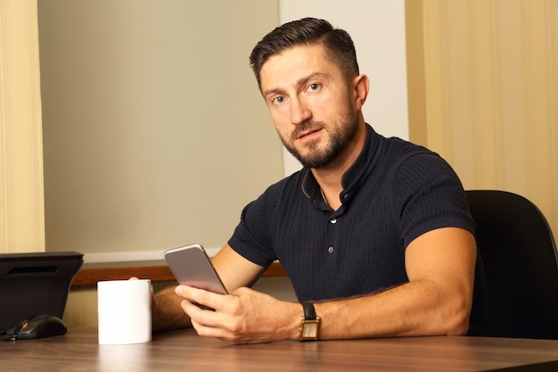 Business man with cup and cell phone in hand sitting at the table