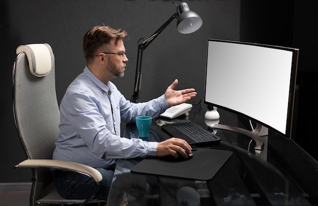 Деловой человек в очках работает в офисе за компьютерным столом и пьет кофе из яркой чашки