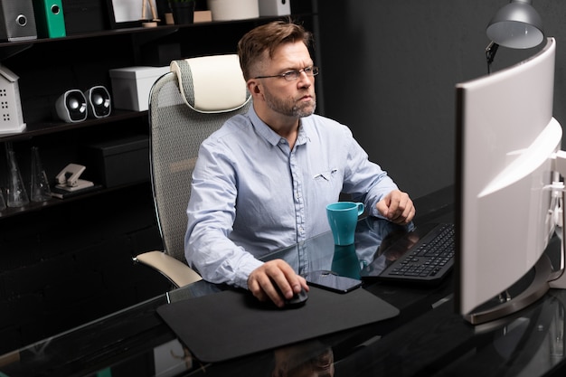 Business man with glasses working in office at computer table and drinking coffee