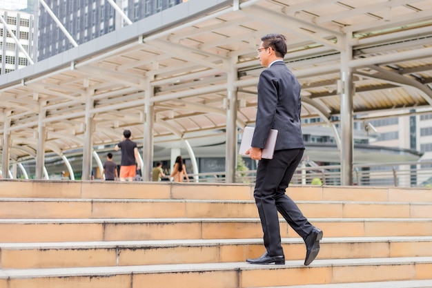 Business man with his laptop going up the stairs  in a rush hour to work